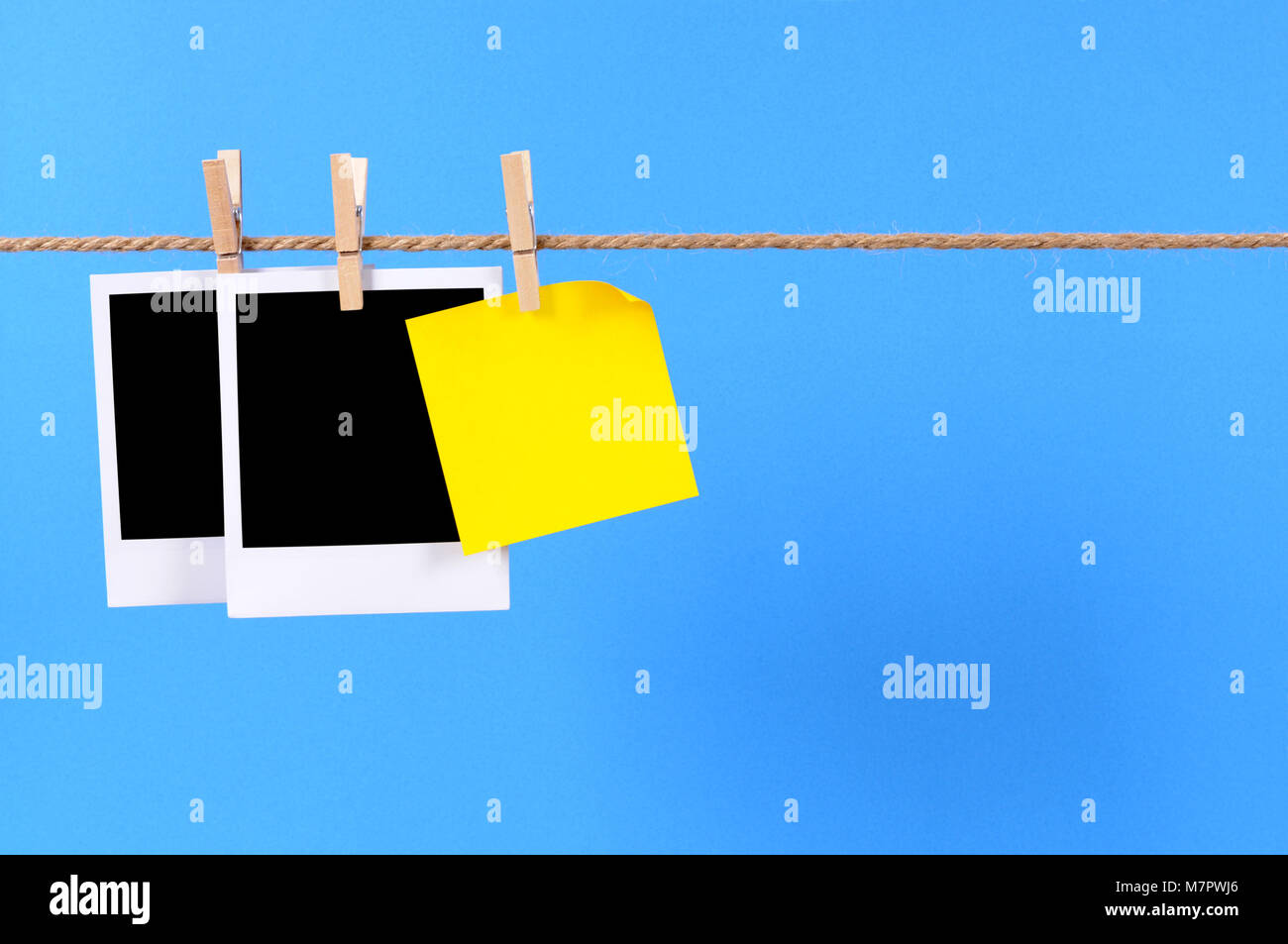 Blank instant camera photo prints and an office sticky note hanging on a rope or string isolated against a blue background.  Space for copy. Stock Photo
