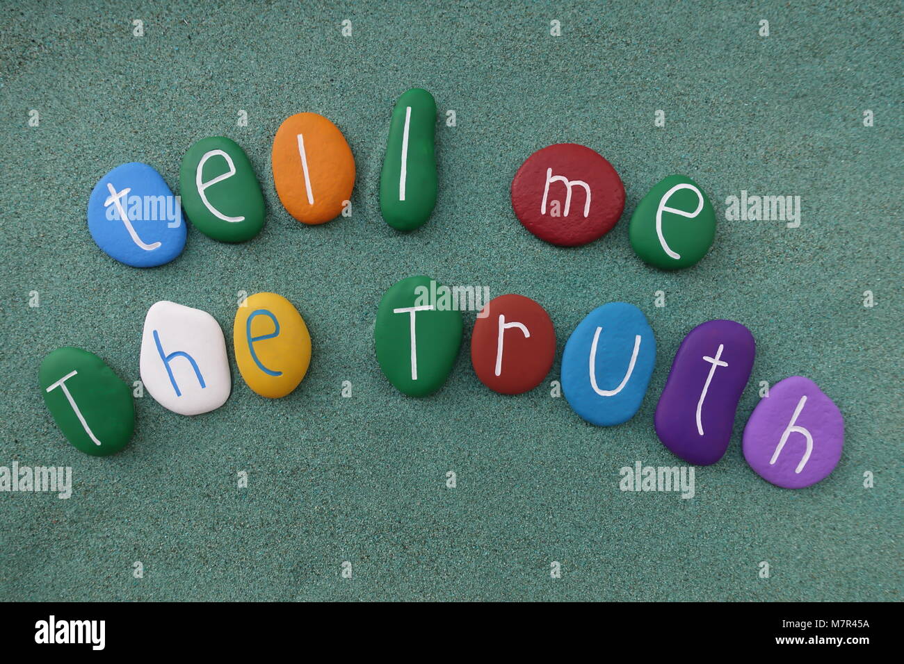 Tell me the truth, multicolored stones text over green sand Stock Photo