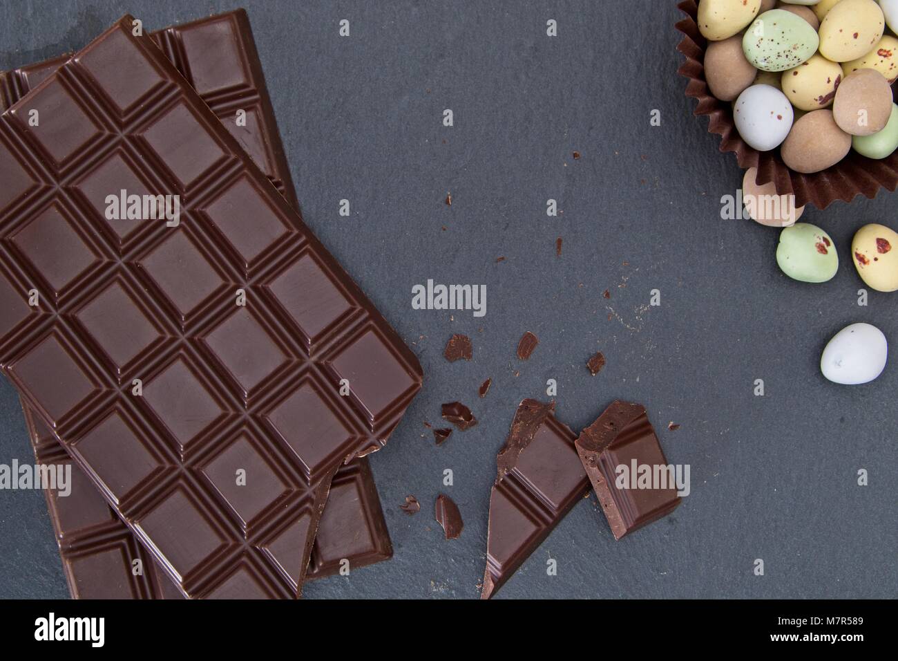 Broken plain chocolate and mini chocolate eggs on slate Stock Photo
