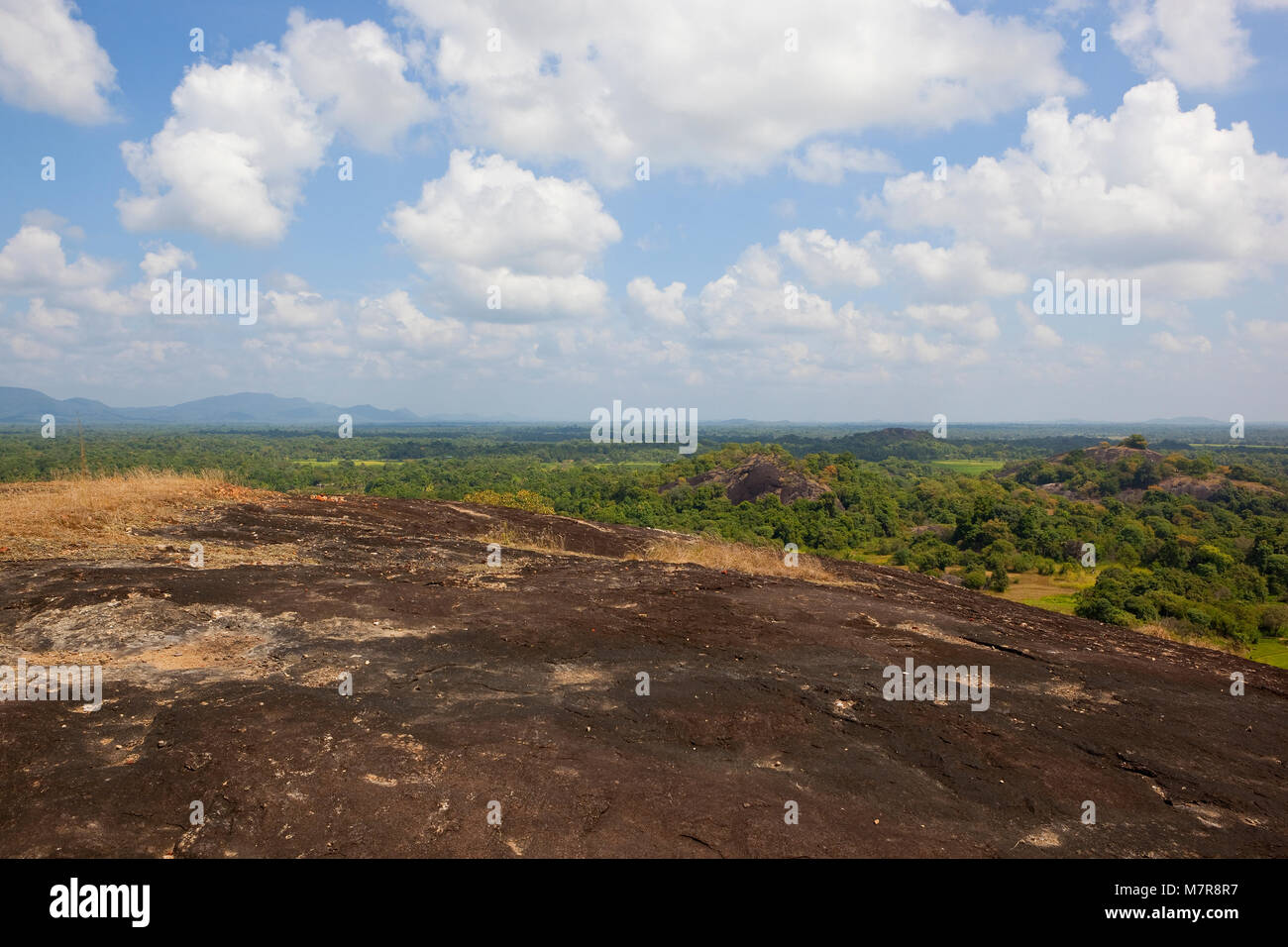 volcanic rock overlooking a sri lankan scenic vista with woodland and mountains under a blue sky with fluffy white clouds Stock Photo