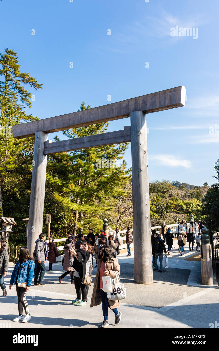 Japan, Ise Grand Shrine, Naiku, inner shrine. Torii gate and bridge leading over river to shrine, many people walking through. Daytime, winter. Stock Photo