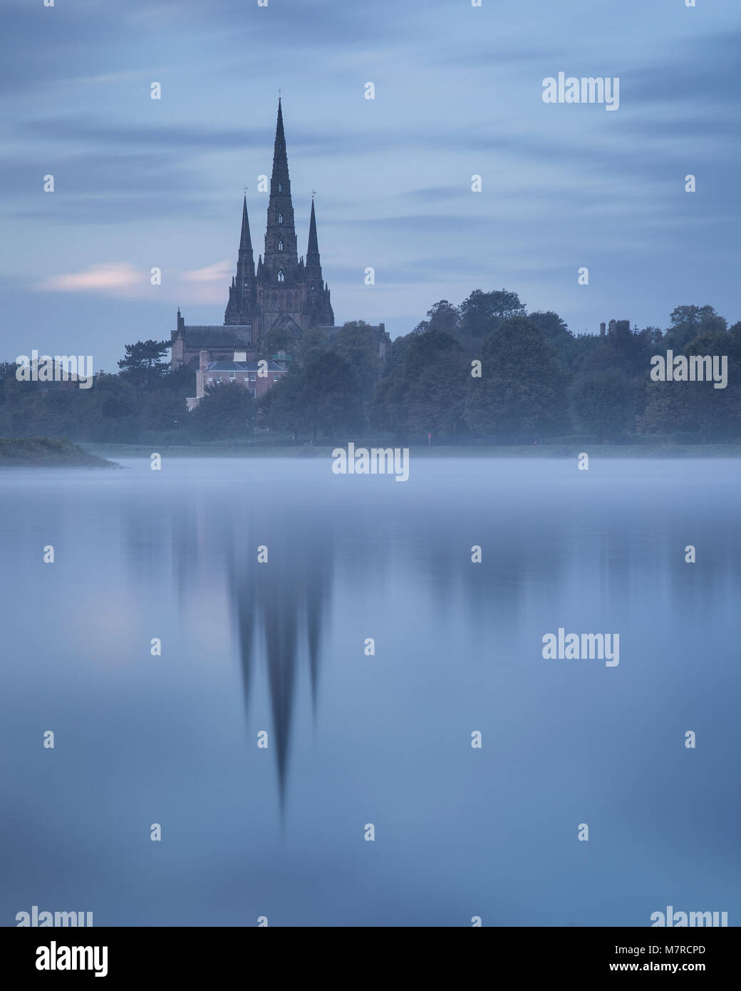 Lichfield cathedral and trees at dawn reflecting in misty lake Stock Photo