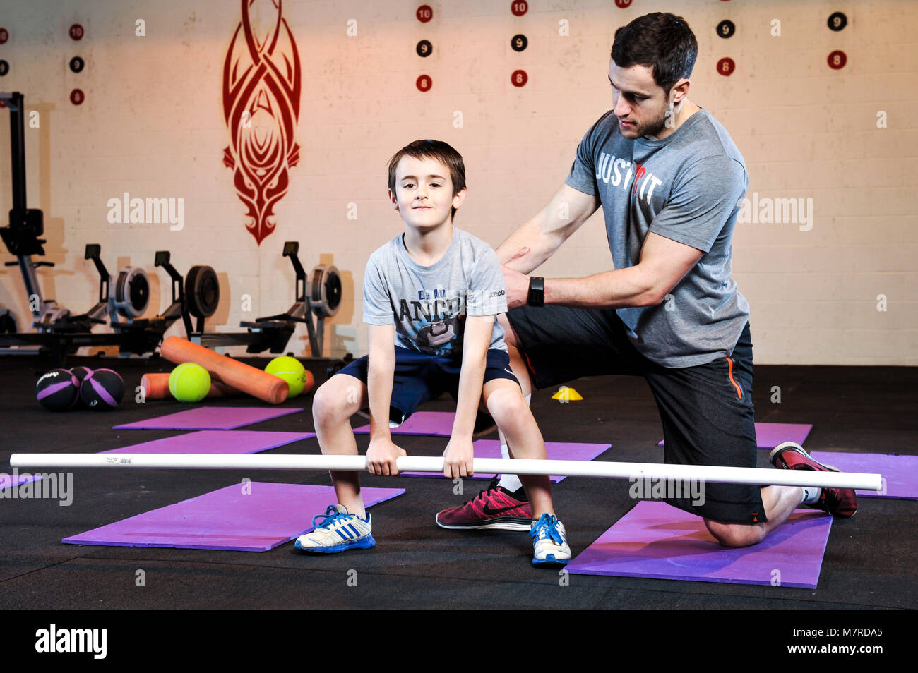 A young boy lifting a weights bar under the supervision of a  gym instructor. Showing how to lift properly Stock Photo