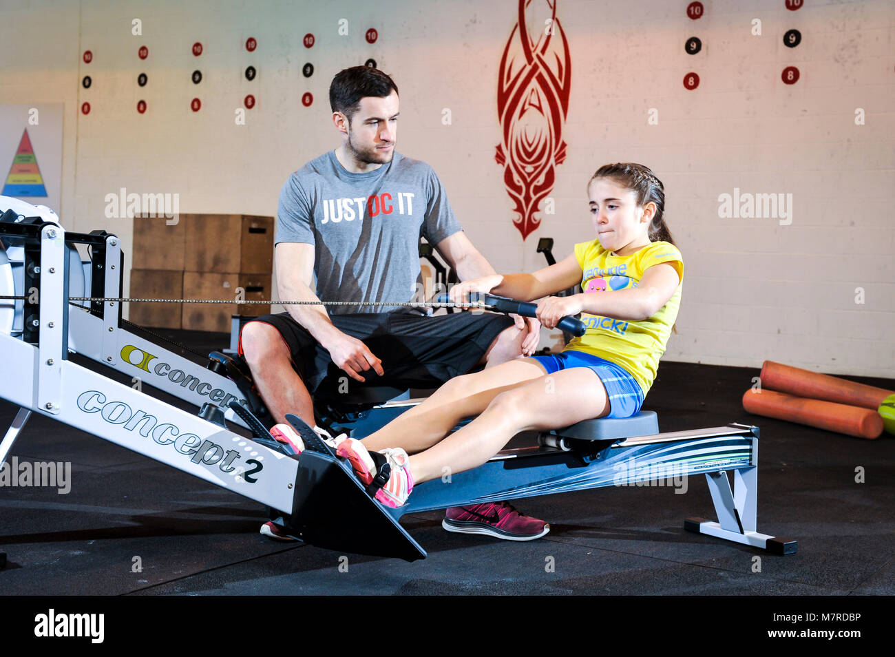 A young girl been given a lesson on a rowing machine in a gym. Stock Photo