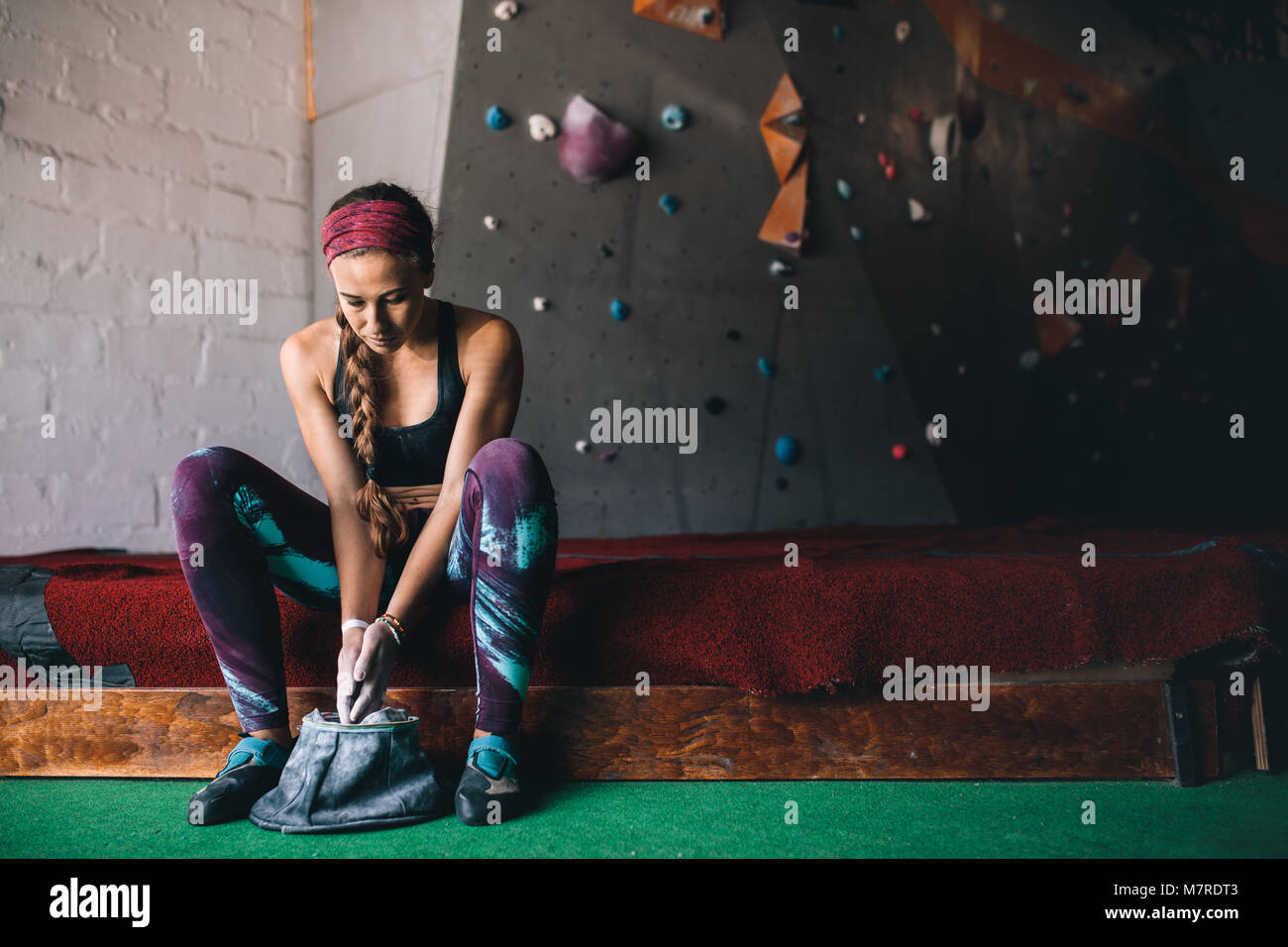 Woman at a wall climbing gym applying magnesium chalk powder on hands from a bag. Artificial bouldering wall in the background. Stock Photo