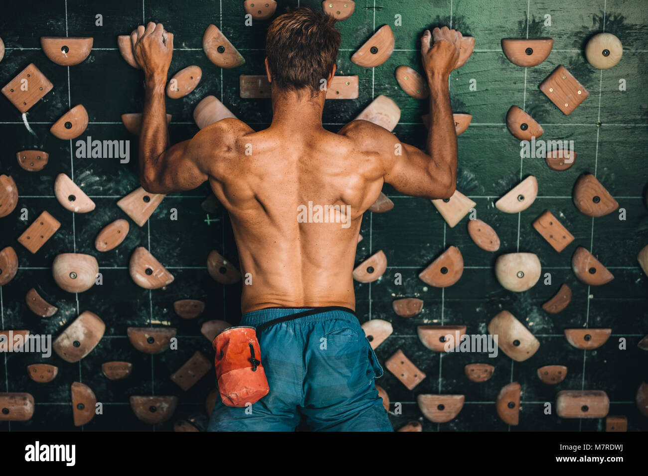 Muscular man climbing wall at an indoor wall climbing centre. Rock