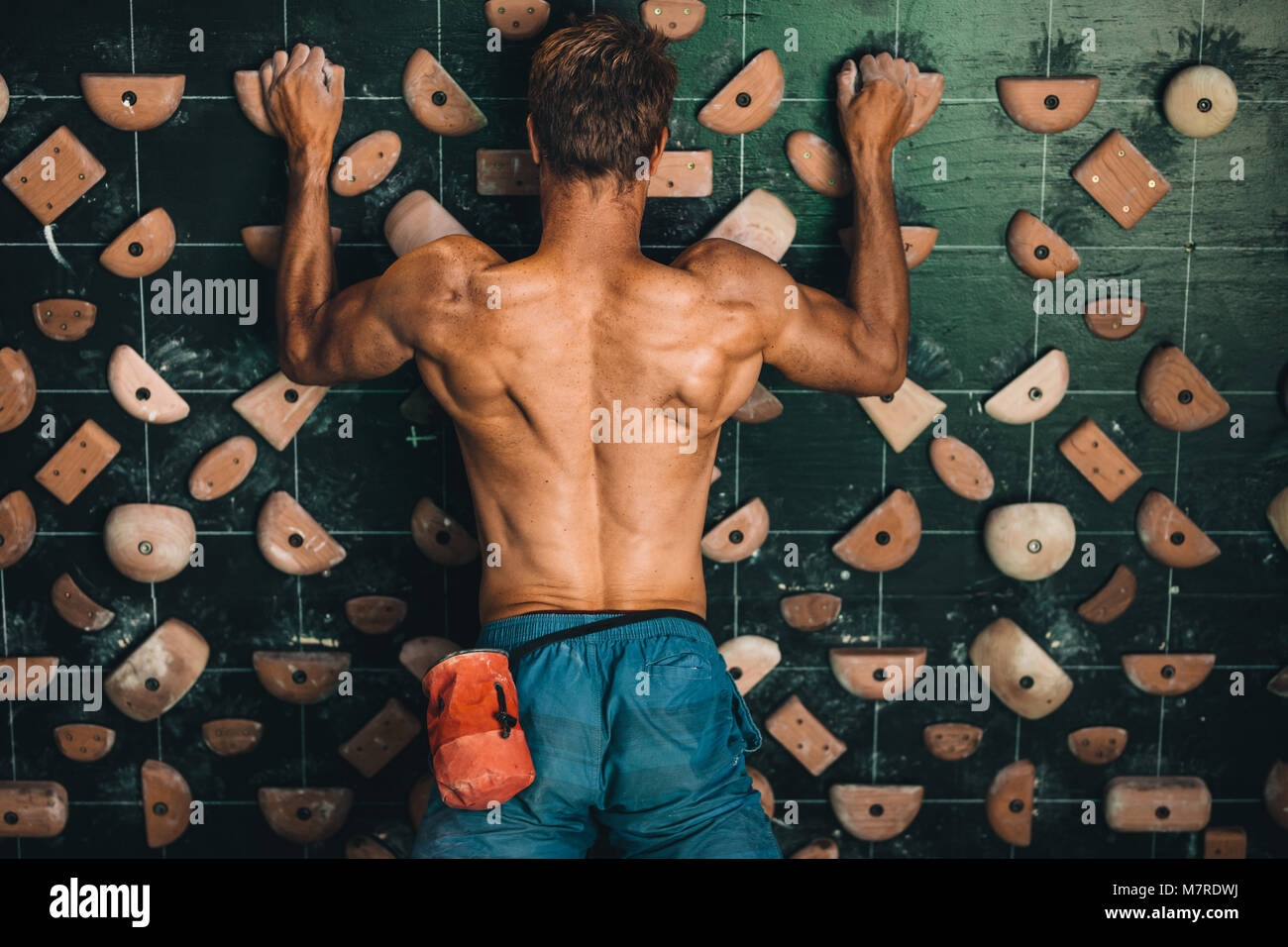 Muscular man climbing wall at an indoor wall climbing centre. Rock climber practicing climbing at an indoor climbing gym. Stock Photo
