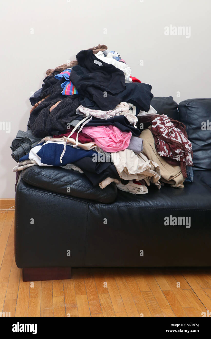 Large pile of messy colorful wardrobe on black leather couch Stock Photo