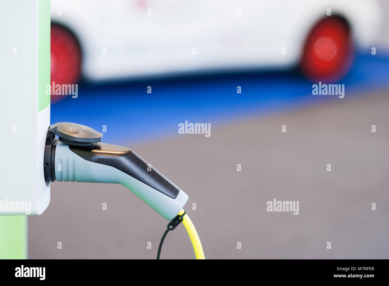 Electric car concept - closeup of the plug for charging on charge station with car in the background - selective focus with room for copy text. Stock Photo
