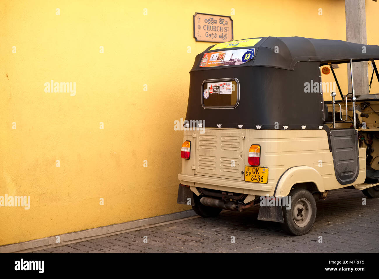 A beige coloured tuk tuk taxi against a yellow wall in Galle Fort in Sri Lanka Stock Photo