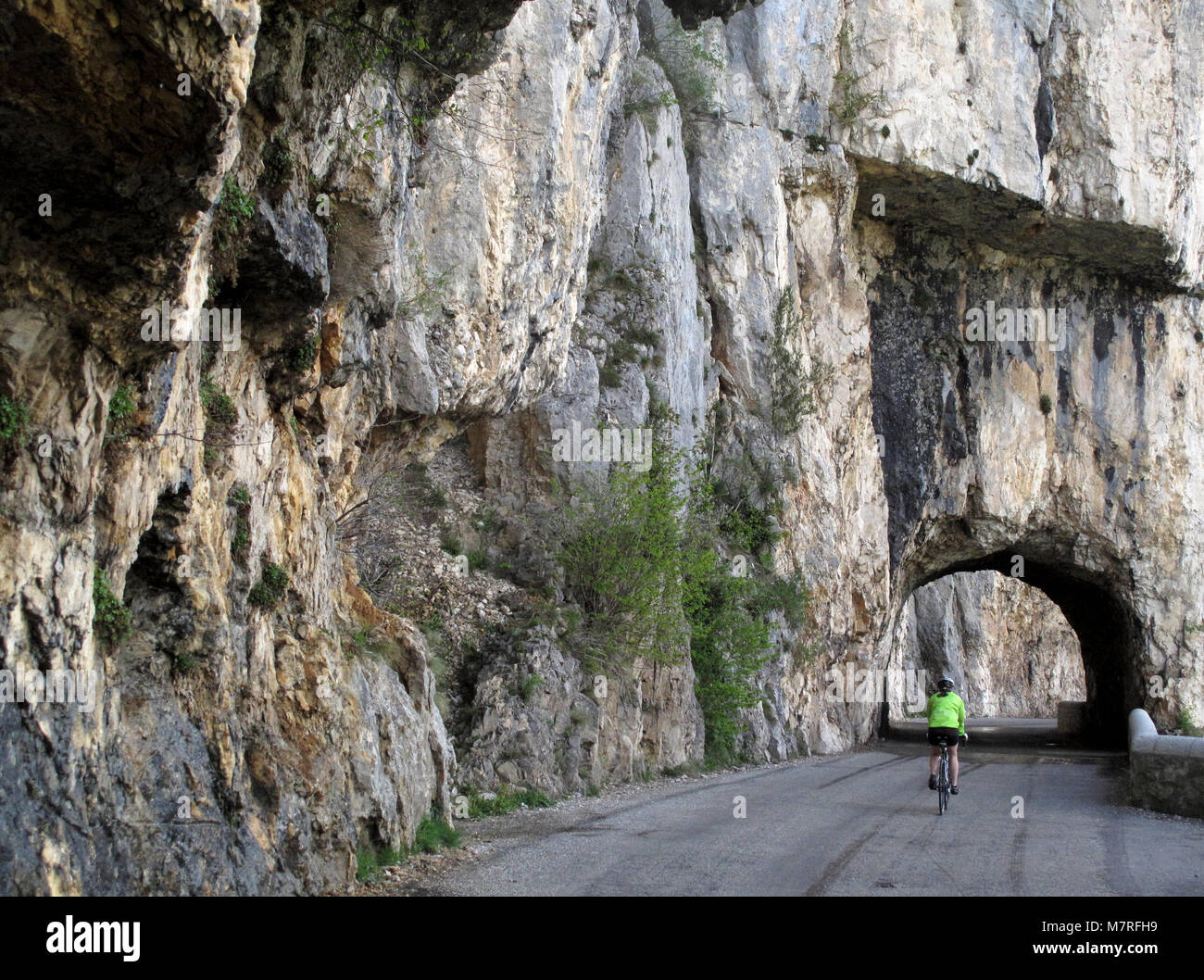 A cyclist approaches a tunnel on the road forming the Cirque de Combe Laval in the Vercors region of the French Alps Stock Photo