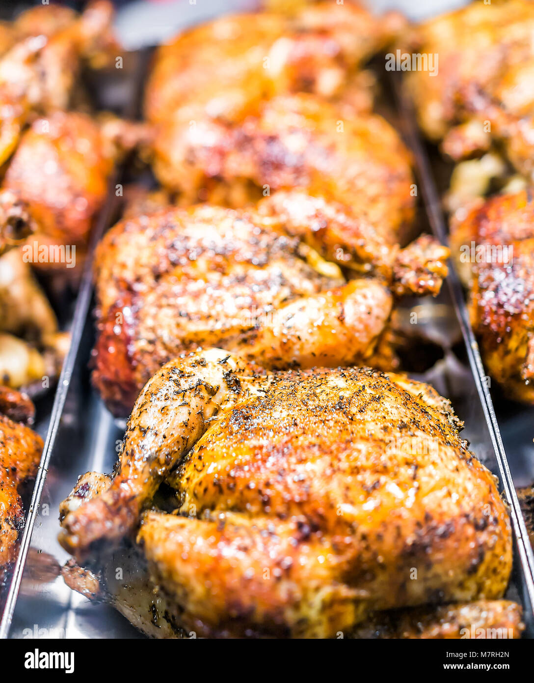 Many roasted whole chicken closeup on tray in deli store shop grocery display brown with herbs, spices, crispy golden skin Stock Photo