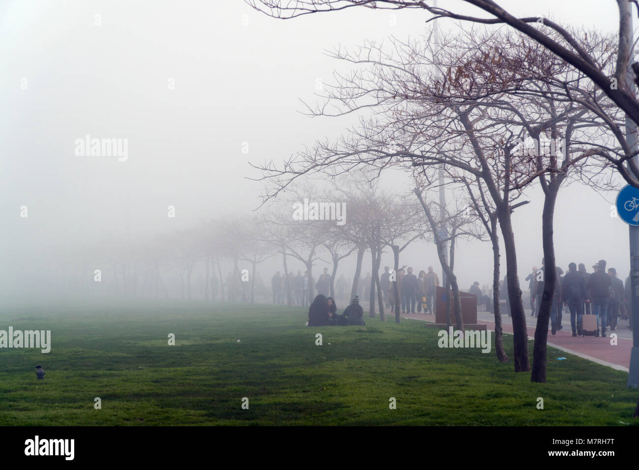 Istanbul, Turkey - March 10, 2018 : A cold foggy weekend at Istanbul, Kadikoy. Many people are walking at the park and three teen girls are sitting. Stock Photo