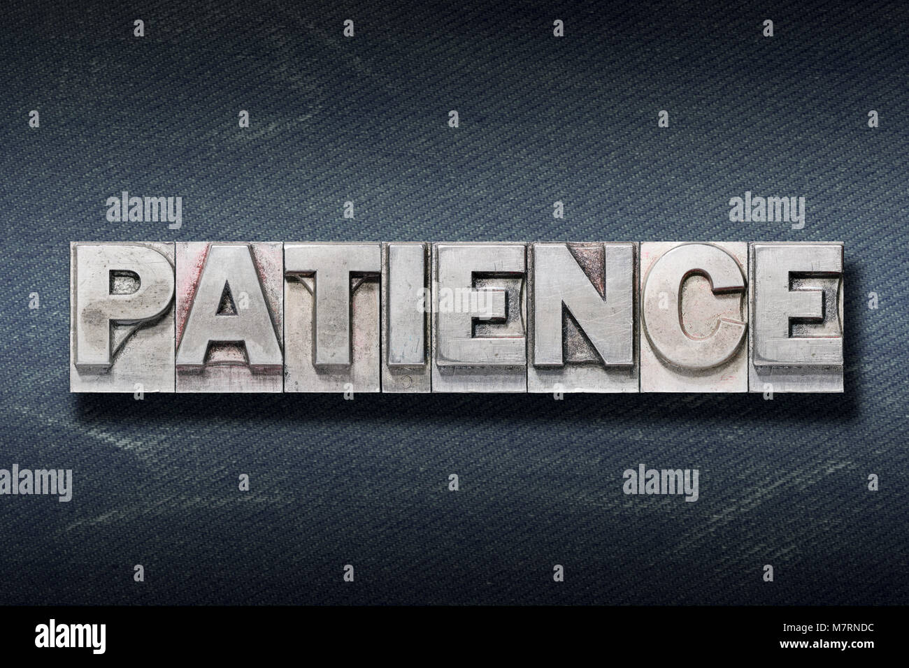 patience word made from metallic letterpress on dark jeans background Stock Photo