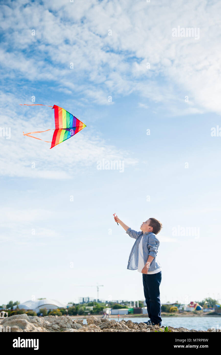 cute little boy playing toy kite flying high in blue sky near sea coast resort Stock Photo
