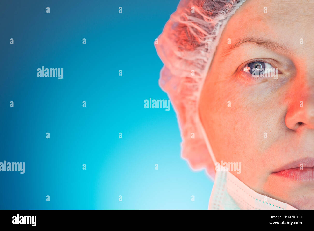 Half face portrait of female medical professional with surgical mask and cap looking at camera, copy space for text or graphic Stock Photo