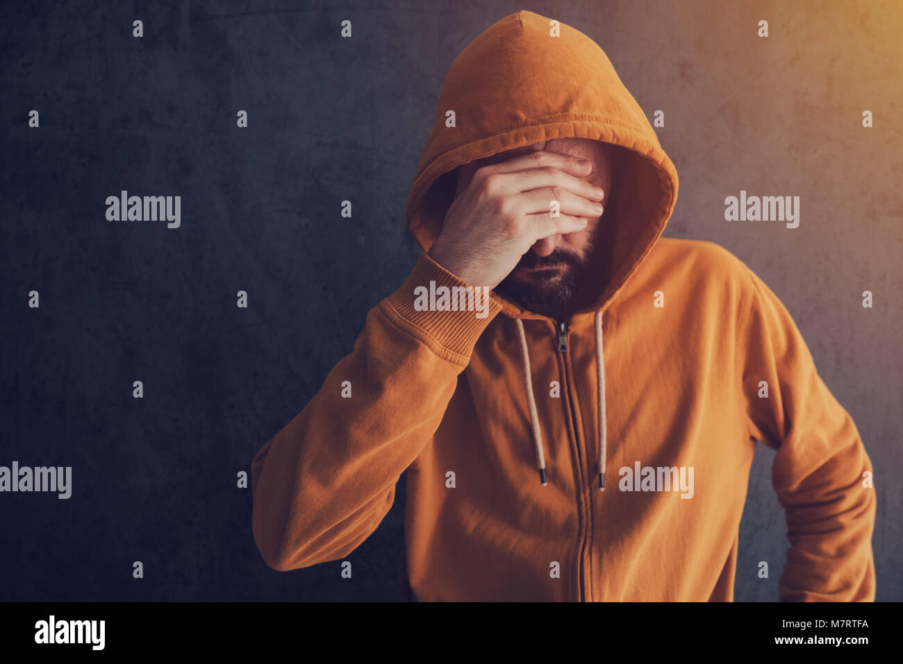 Frustrated hand on forehead, man in yellow hoodie covering face Stock Photo
