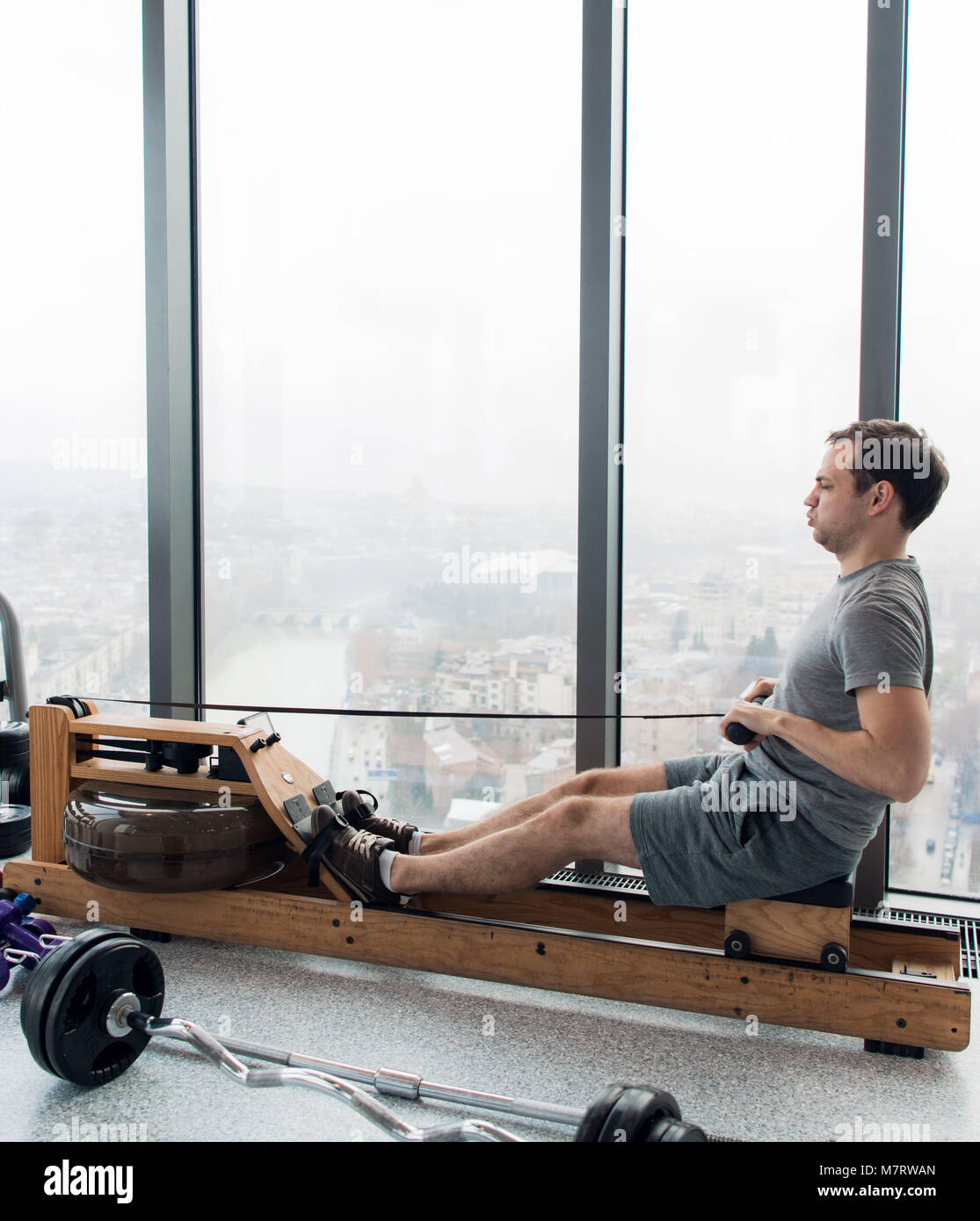 Rowing with power. Side view of young man in sportswear doing rowing in  front of window at gym Stock Photo - Alamy
