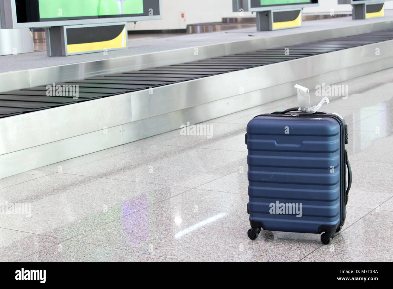 A forgotten lost suitcase in the airport hall. One case stands on wheels at the luggage transporter belt. Stock Photo