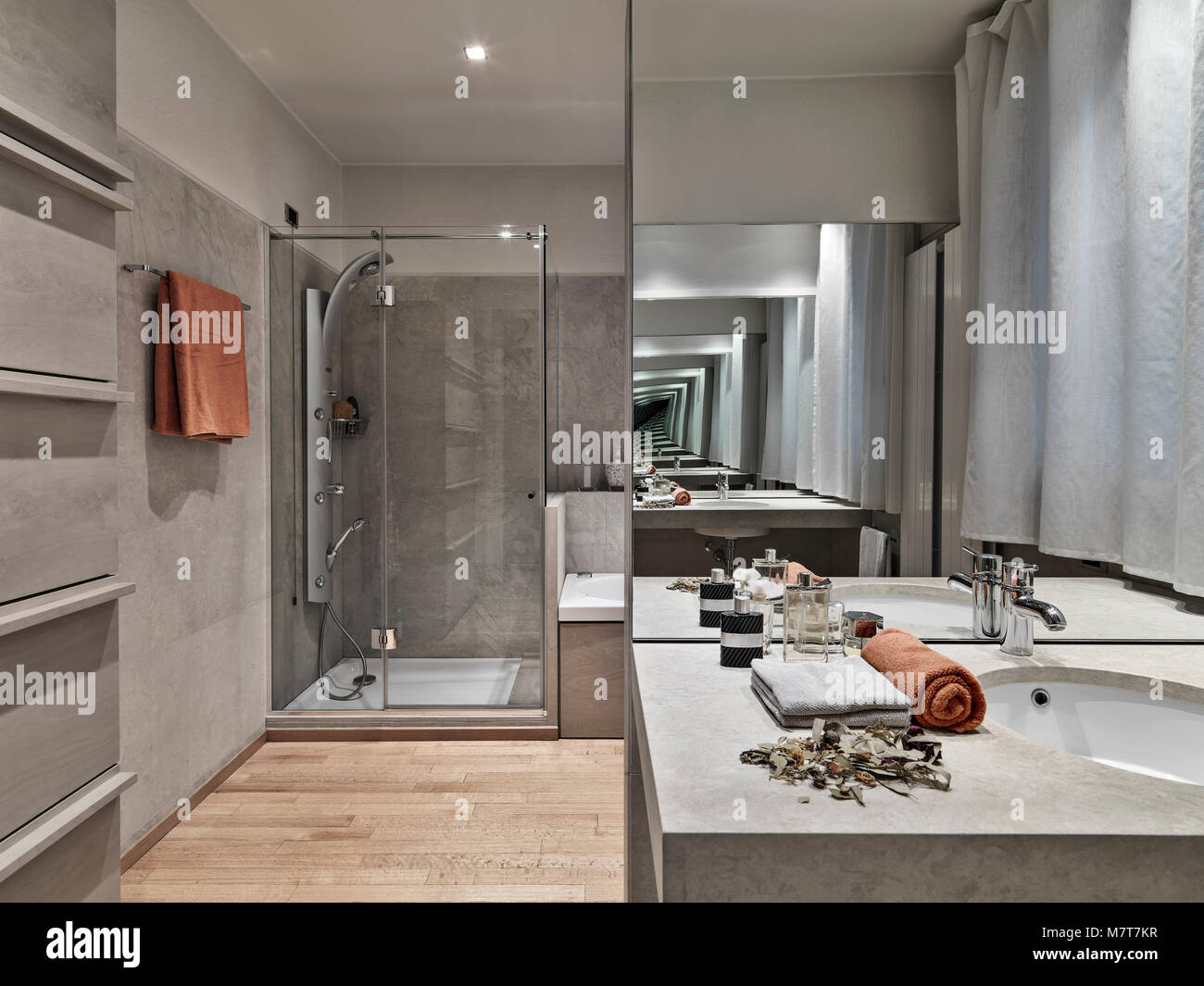interiors shots of a modern bathroom in foreground the built-in washbasin and big mirror on the background the masonry shower cubicle with glass door, Stock Photo