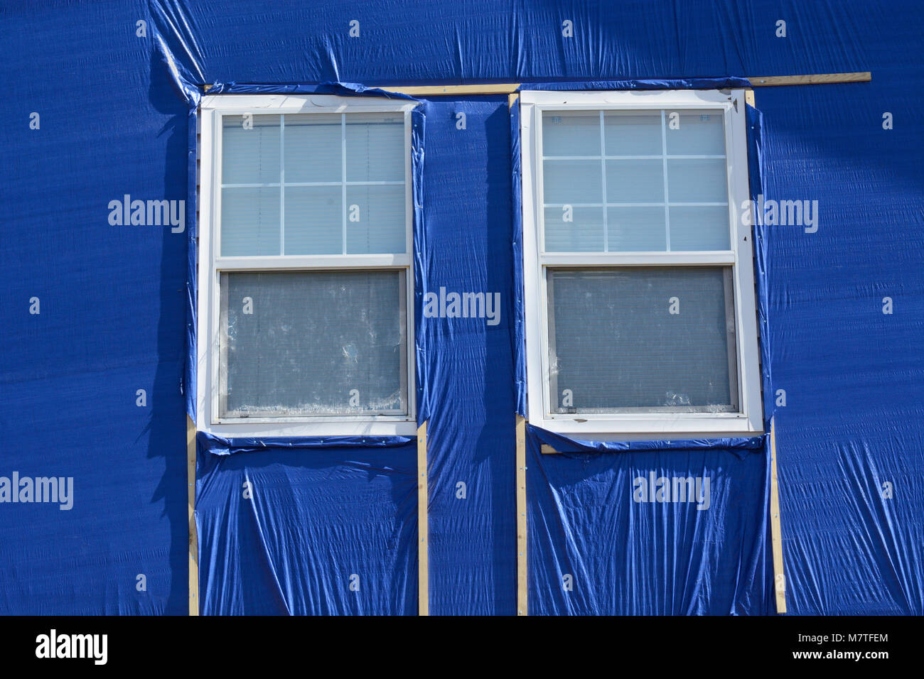 Hail storm damage repair with blue cloth covering broken house siding