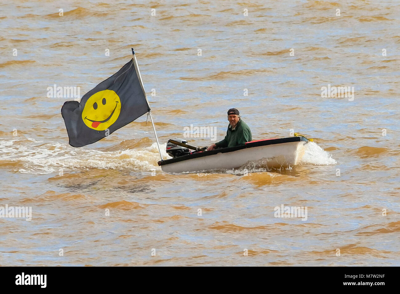 Sidmouth, Devon, UK.  13th March 2018.  UK Weather.  A man in a boat flying a large flag as he sails near to the beach at the seaside town of Sidmouth in Devon on a warm sunny spring afternoon.  Picture Credit: Graham Hunt/Alamy Live News. Stock Photo