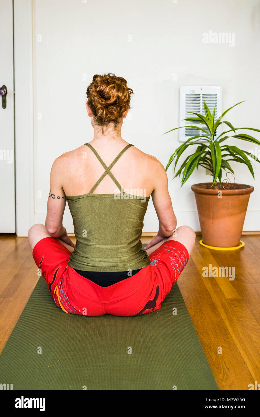 A Young Woman Seen From Behind Seated In Sukhasana Pose On Her