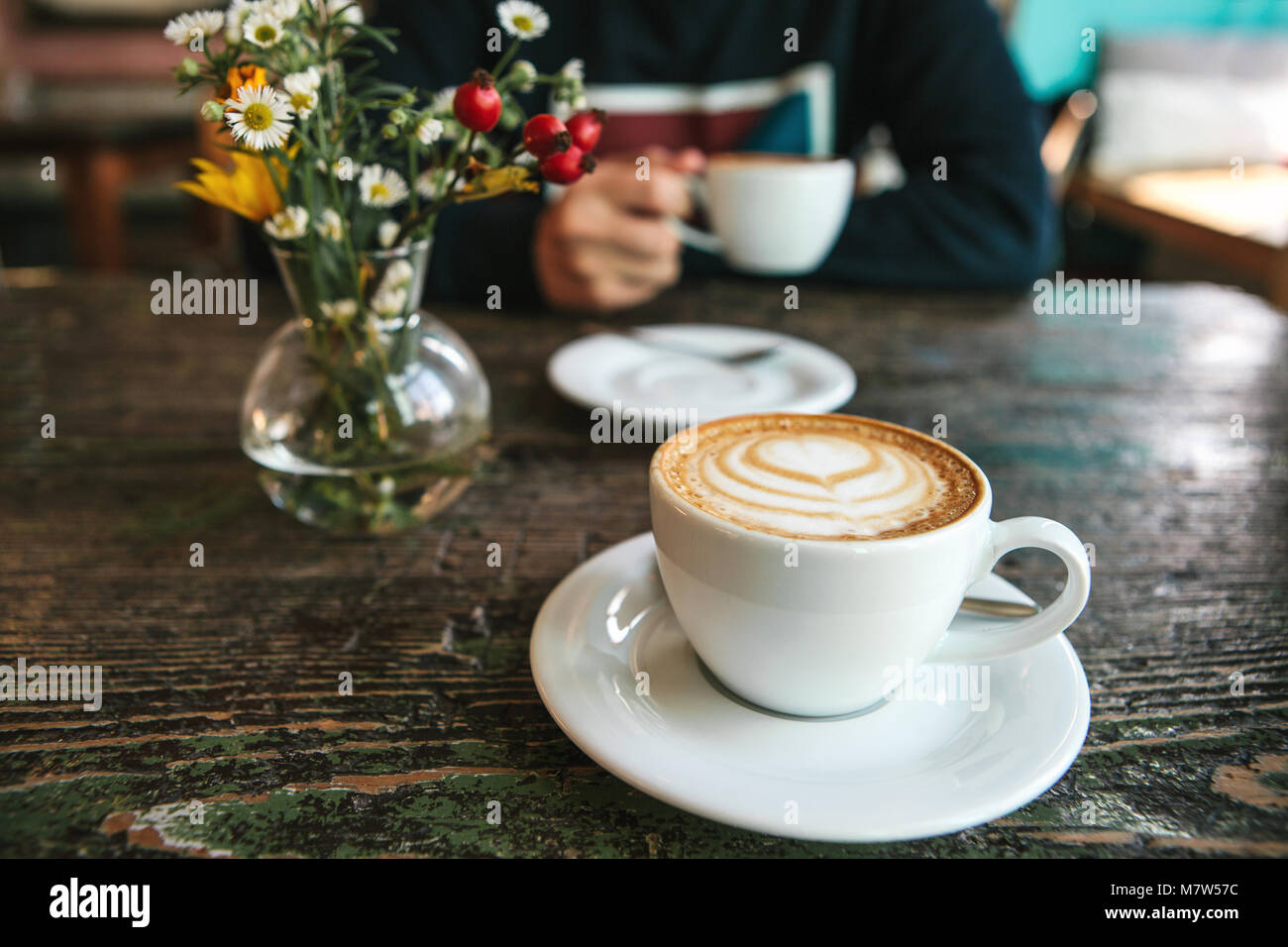 Two cups of coffee and a vase of flowers on a wooden table, the ...