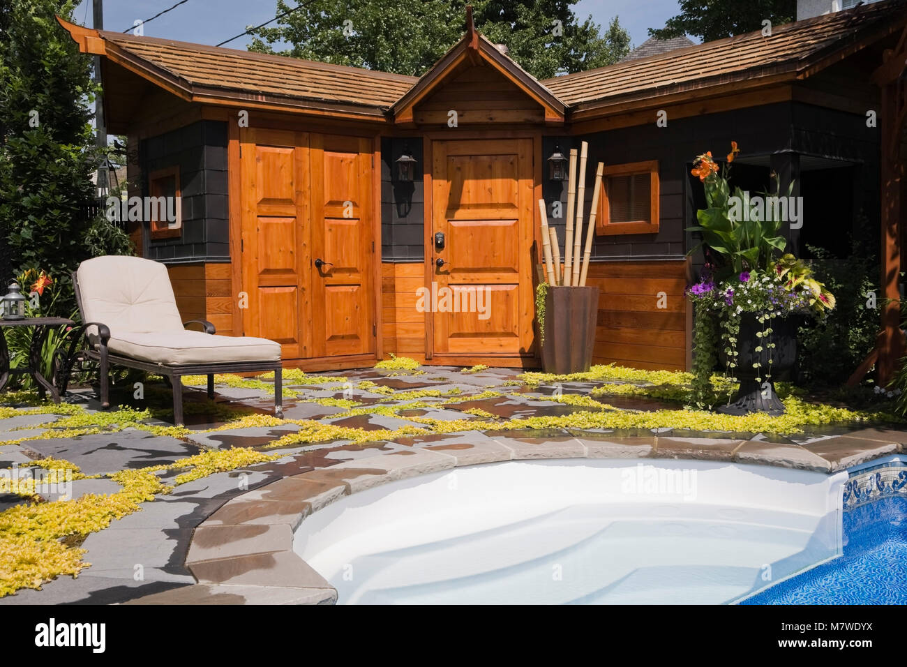 Long chair on patio stones next to a storage shed in a landscaped residential backyard in summer. Stock Photo
