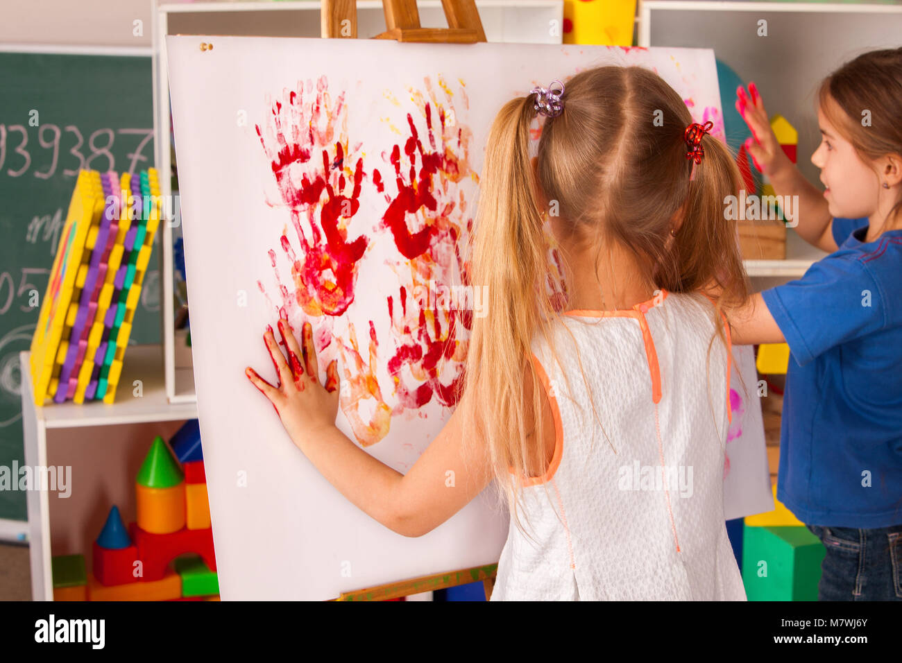 Children painting finger on easel. Group of kids with teacher. Stock Photo