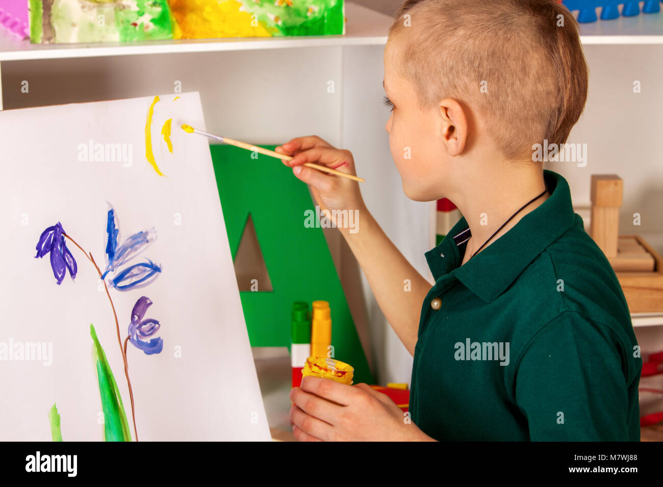 Child painting finger on easel. Kid boy learn paint school. Stock Photo