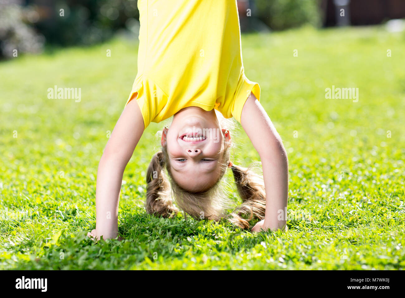 Happy little girl standing on her head on green lawn Stock Photo - Alamy