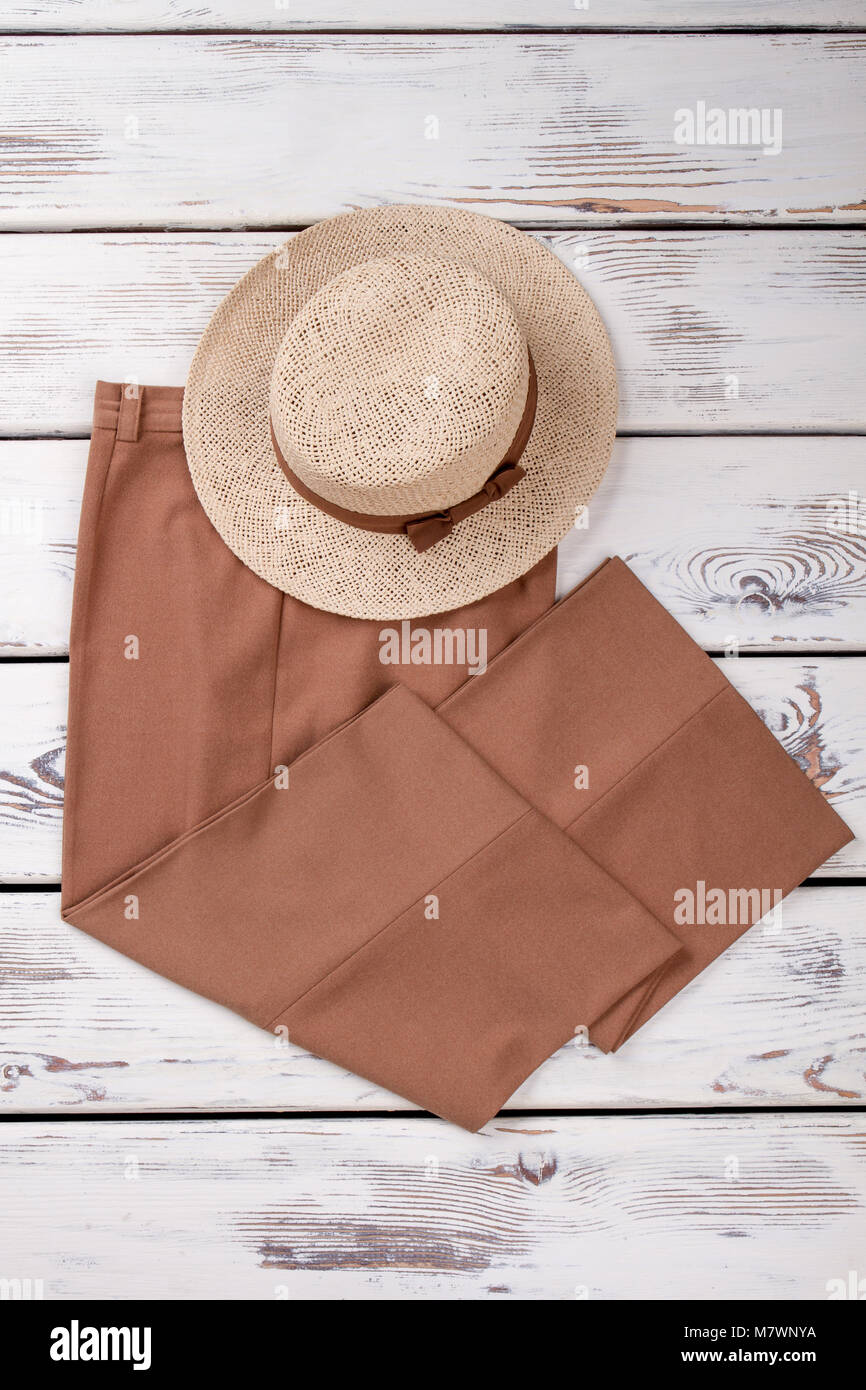 Flat lay brown trousers and summer hat. Bright wooden desks surface background, vertical view. Stock Photo