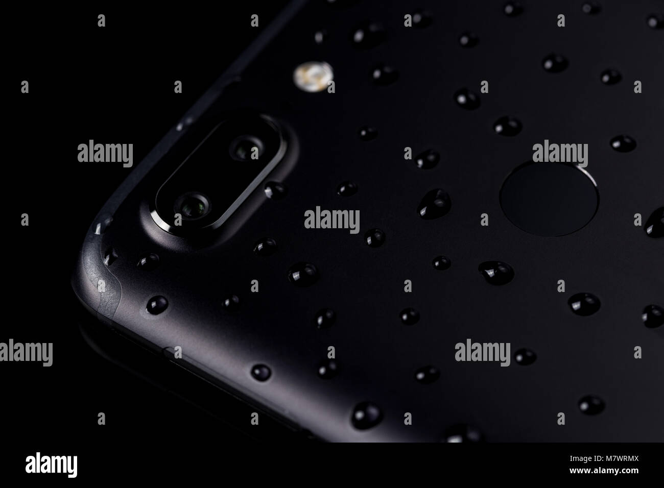 Close-up of water drops on black smartphone with dual camera , flash and fingerprint sensor on black backgr Stock Photo