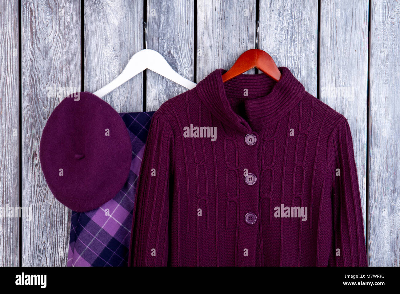 Purple winter outfits for girls. Flat lay, wool cardigan, hat and skirt. Dark wooden desk surface background. Stock Photo