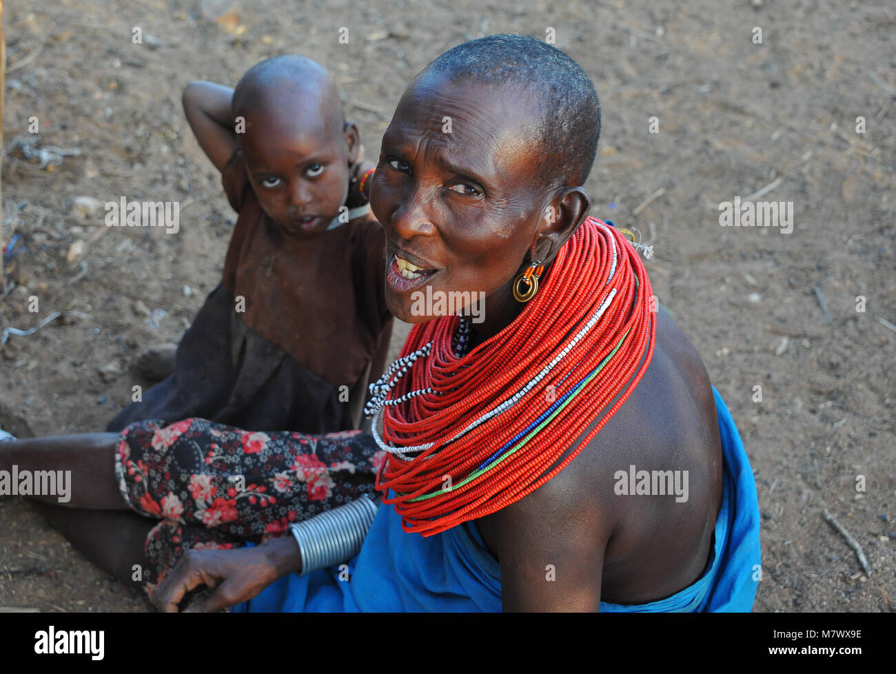 Portrait of an unidentified mother and child, wearing traditional ornamental necklace of red beads, sits outside hut in local village. Stock Photo