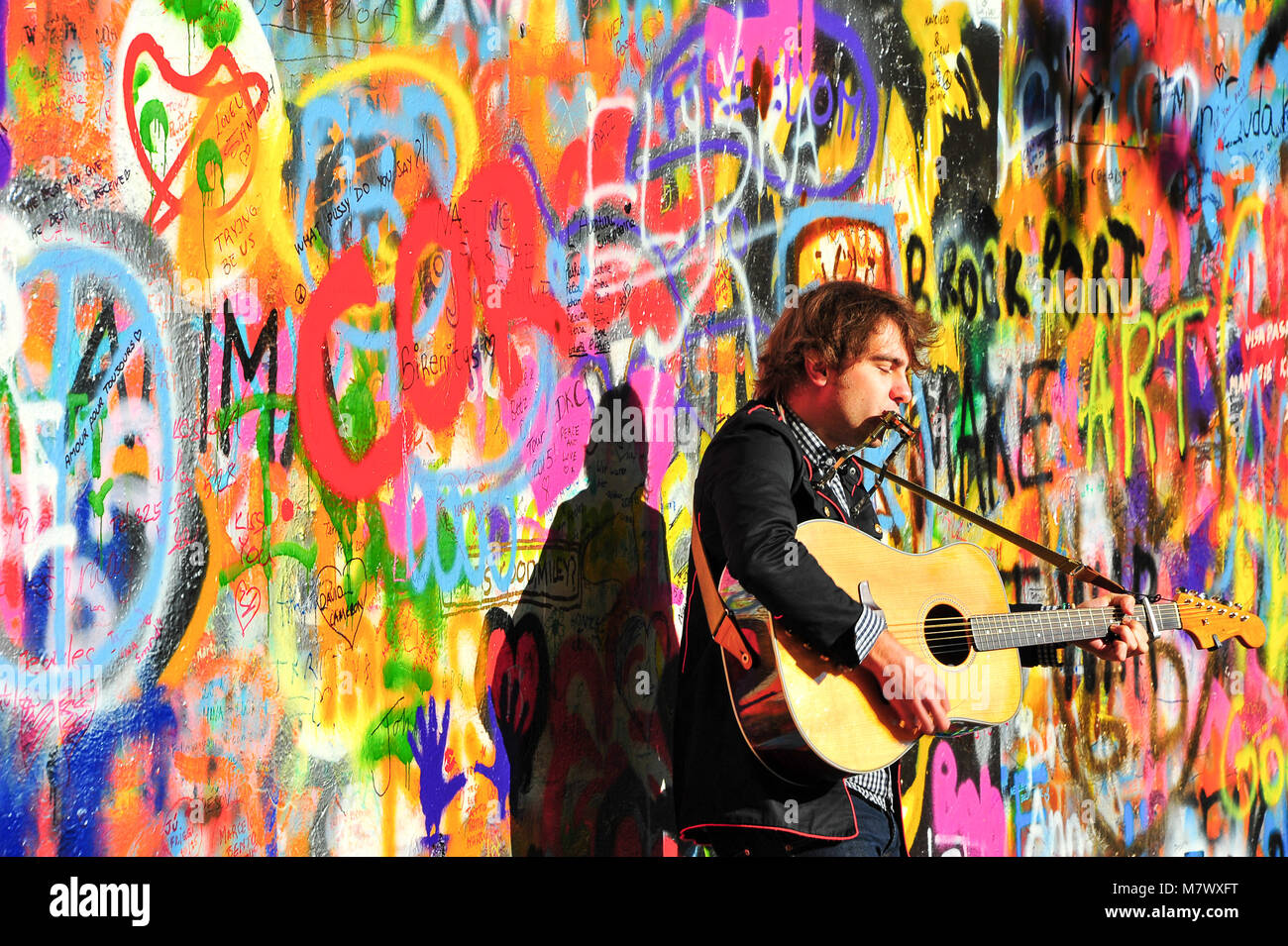 Street busker performs Beatles music at the John Lennon Wall on Kampa Island. in Prague. Musician with guitar in front of colourful graffiti wall Stock Photo