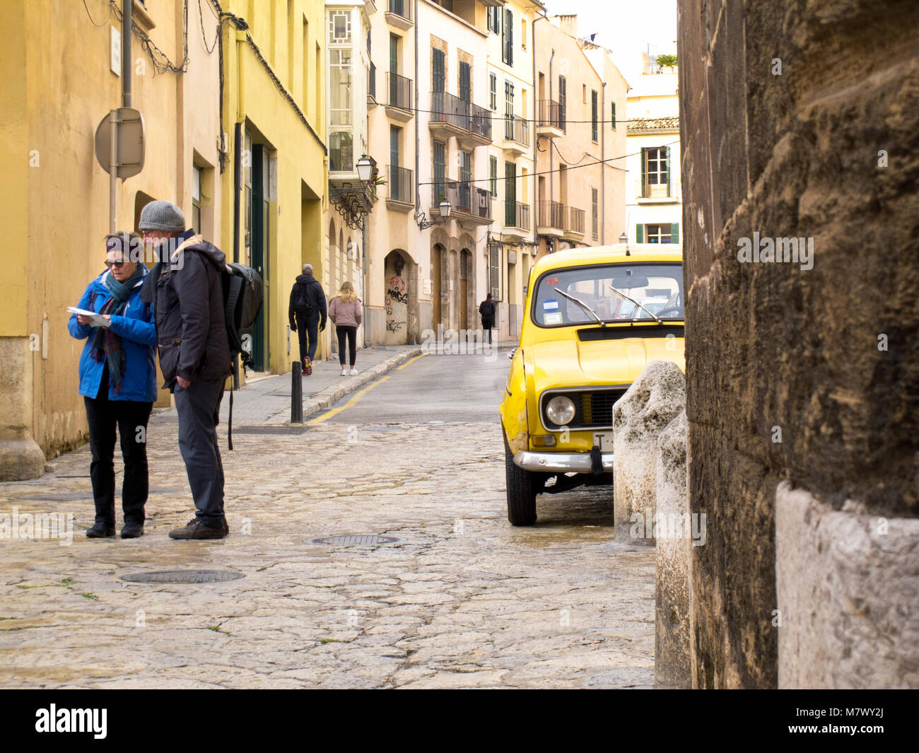 Couple of tourists with hats on looking at map in old cobbled street next to old yellow car Stock Photo