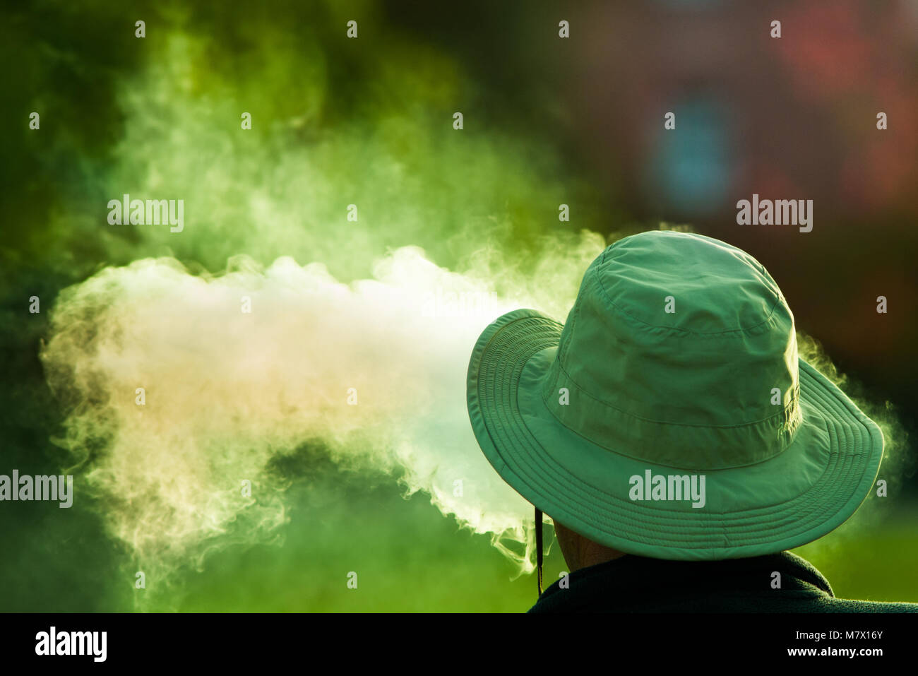 man wearing green hat exhaling poisonous looking green smoke Stock Photo