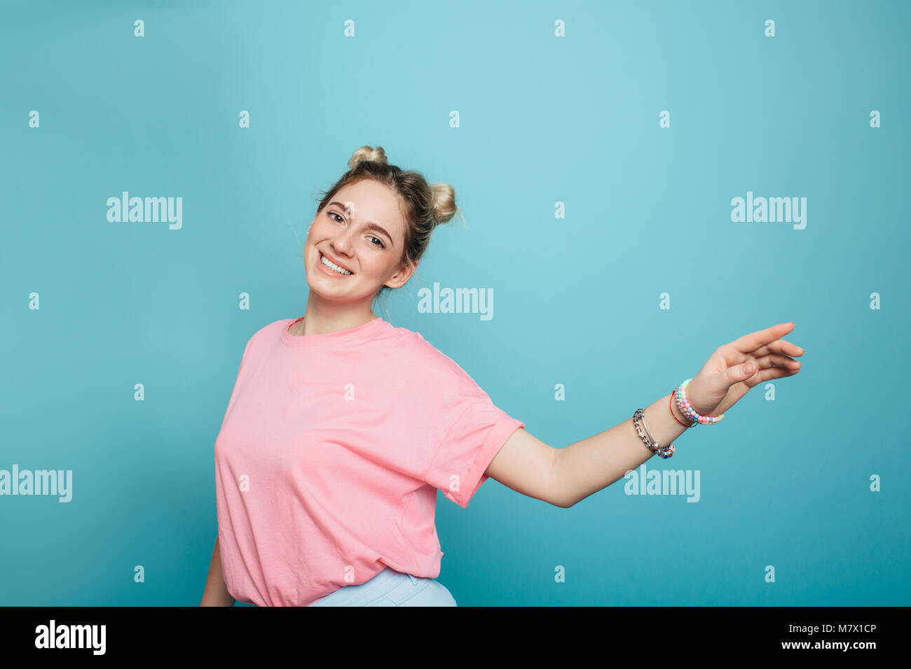 modern young woman with double buns hair waving hand on a blue pastel background Stock Photo