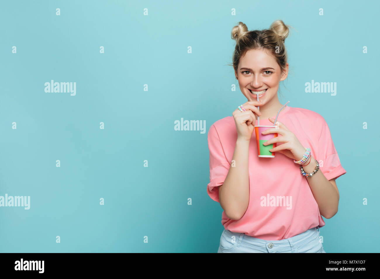modern young woman holding paper cup and drinking beverage with drinking straw on a blue pastel background. party time Stock Photo