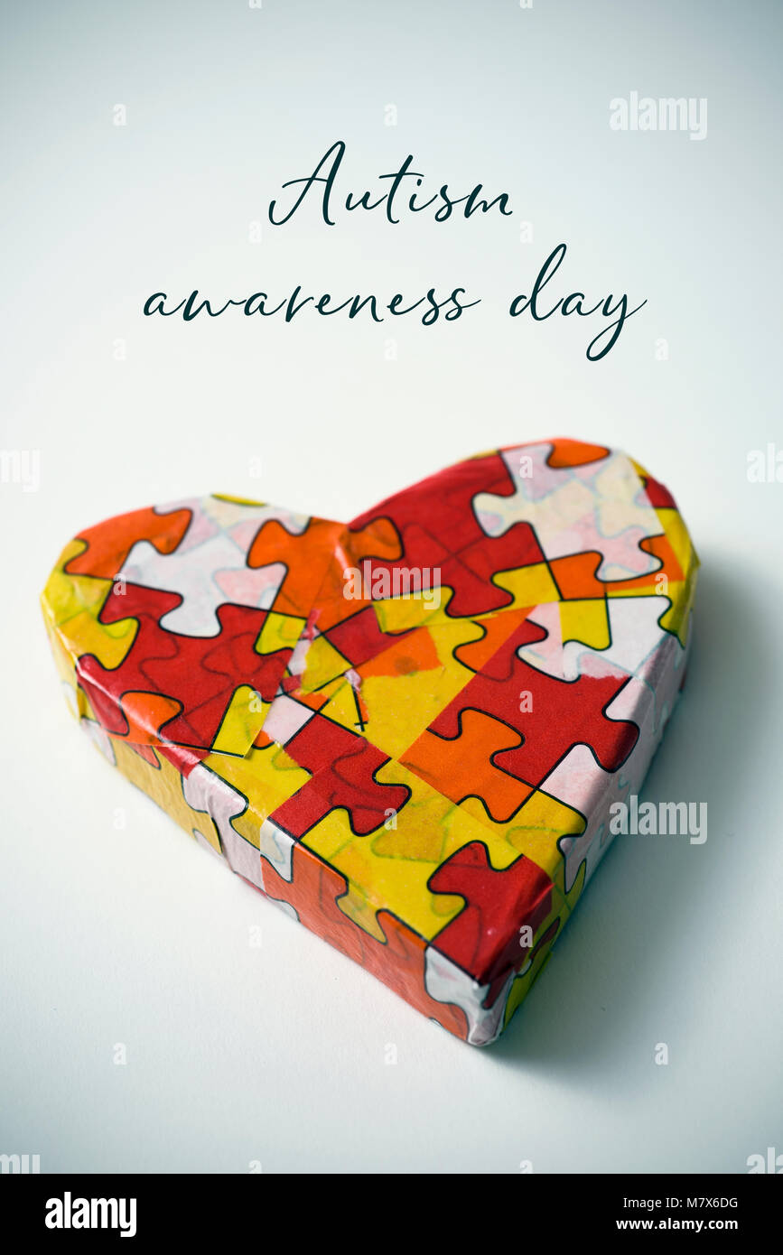 a heart patterned with many puzzle pieces of different colors, symbol of the autism awareness, and the text autism awareness day on a white background Stock Photo