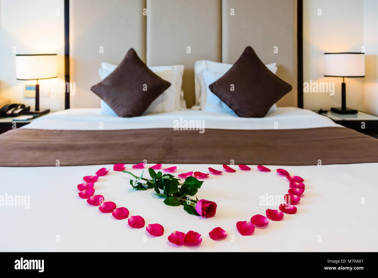 A red rose sits in the middle of a heart made from rose petals on a bed in  a modern hotel room Stock Photo - Alamy
