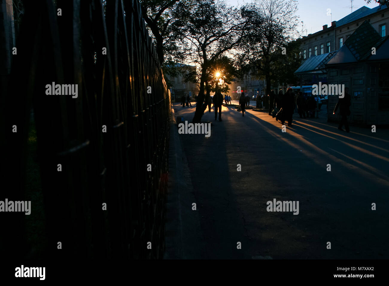 people silhouettes on dark old city street at back-light of sun through ...