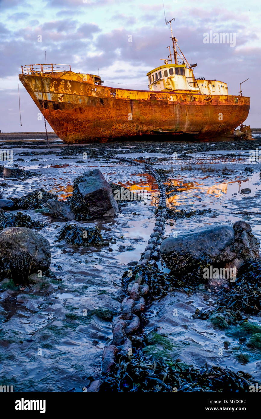 Rusty old fishing vessel marooned at low tide on a mud bank the boats long  big anchor chain goes from the centre foreground to the boat in the backgro  Stock Photo 