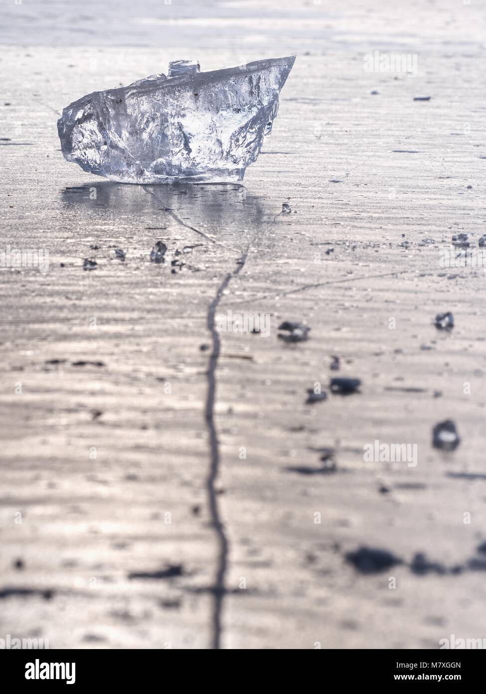 sparkling shards of cracked ice jut out on the frozen lake. The light effect occurs in deep and shallow cracks of sublime ice. Follow the depth of fie Stock Photo