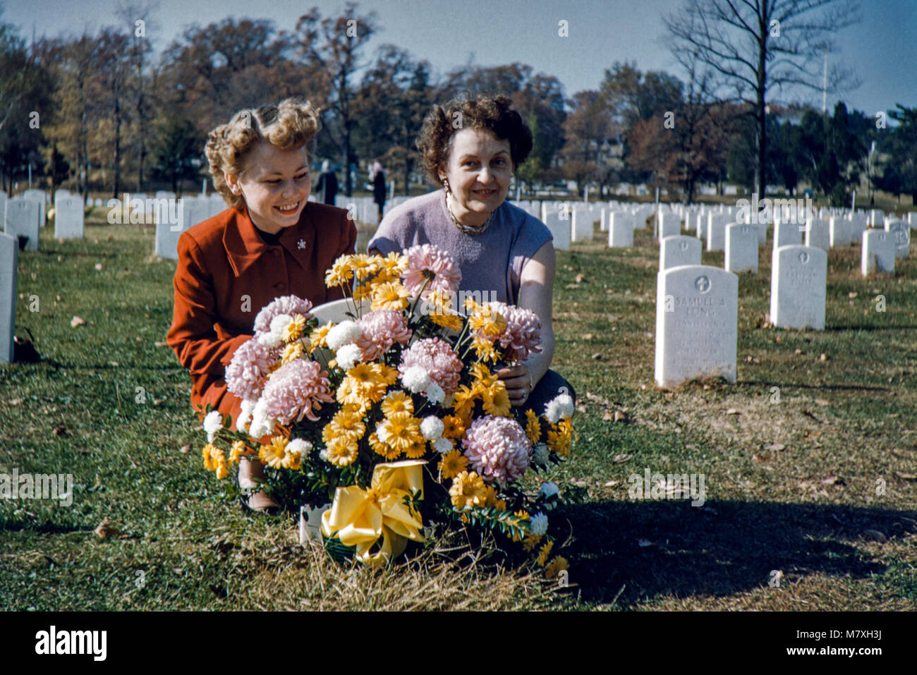 Two women kneel and lay flowers at a loved ones grave. Image taken in
