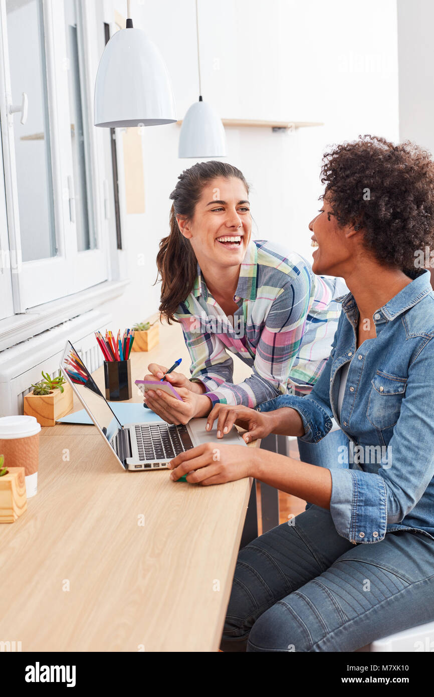 Two young women as colleagues work and laugh together on laptop computer Stock Photo