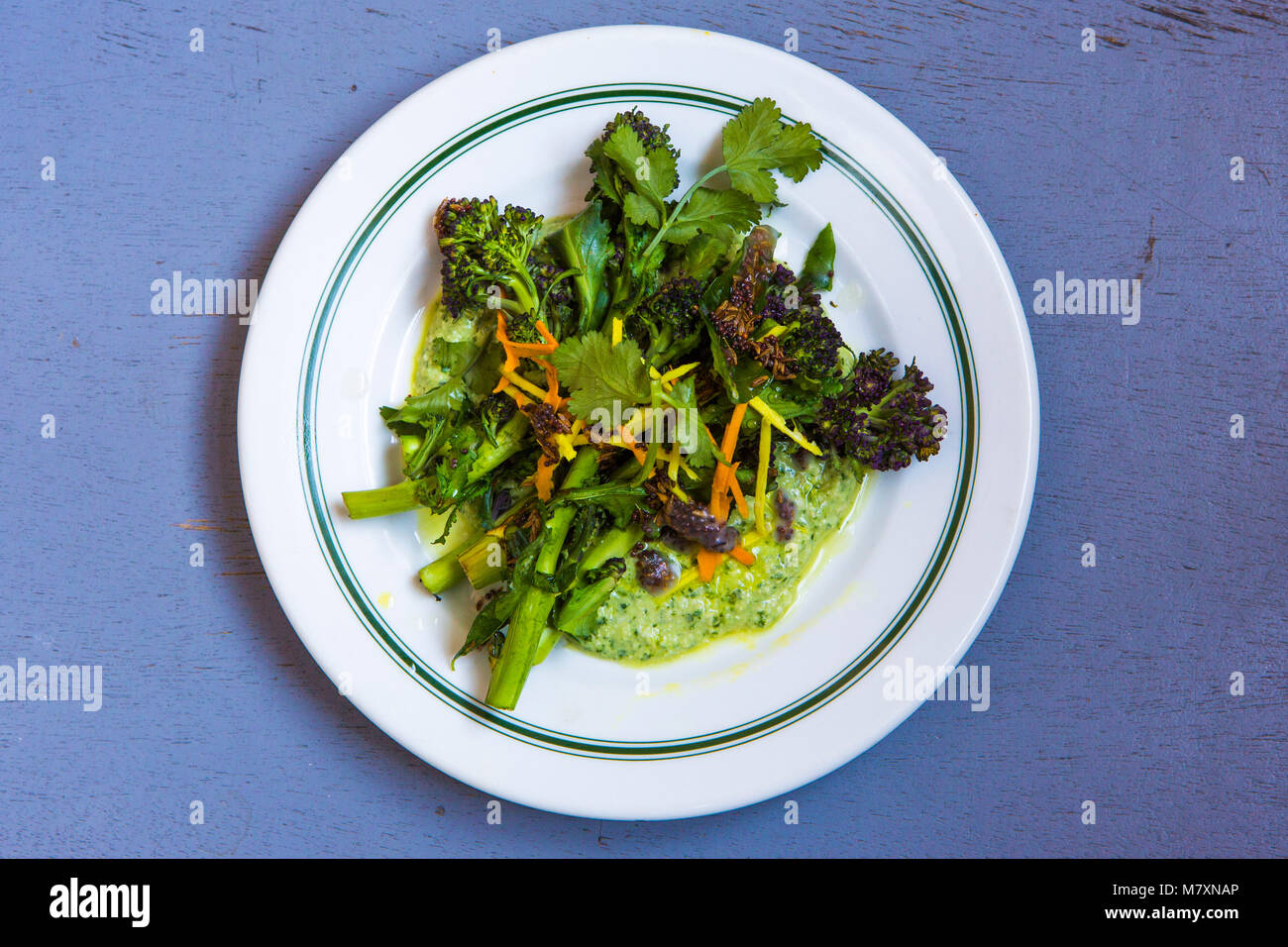 Purple sprouting broccoli thoran with cashew butter on white plate with blue background. Stock Photo
