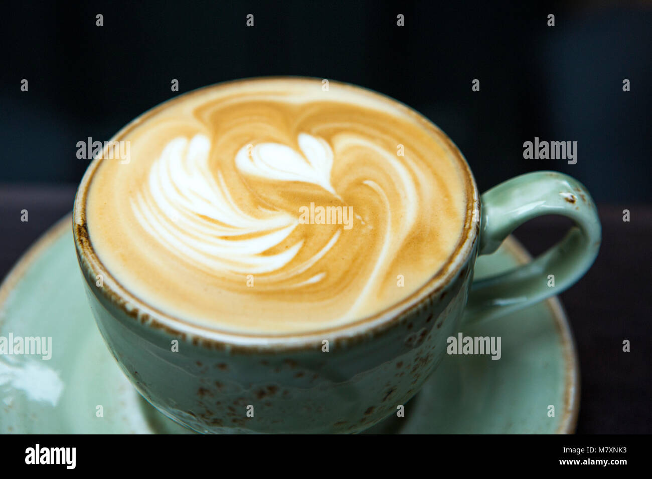 Cappuccino in green coffee cup and saucer with heart. Stock Photo